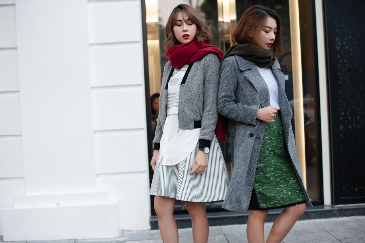Two fashionable women in autumn outfits with coats and scarves on a city street.